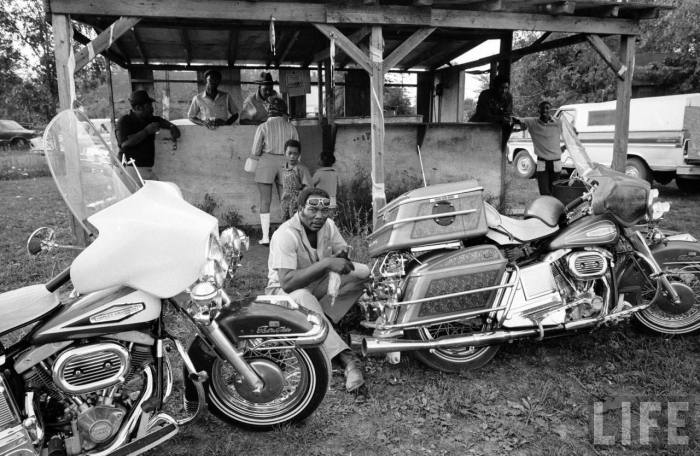 Black motorcyclist of the Big Circle Motorcycle Association sitting between pair of Harley Davidson cruising bikes-- circa 1971.