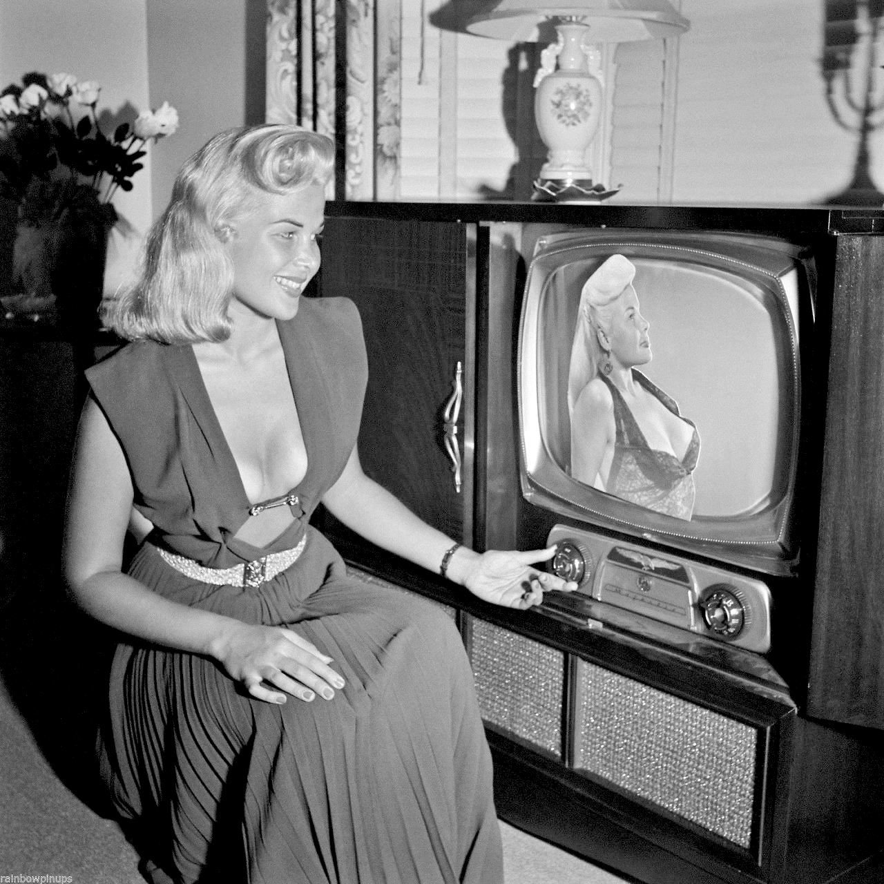 The sexy gloria pall posing in front of a tv with her image, that is actual...